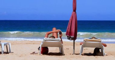 Women relaxing on a deckchair under the sunlight, near the white-sand beach in Philippines. Perfect for relaxing holidays on the beach near water.
