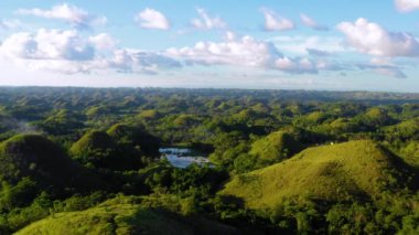 Filipinler, Bohol 'daki Chocolate Hills' te bir evde insansız hava aracı ile hava manzarası. Güzel yeşil tepeler ve ağaçlar ufukta, mavi gökyüzünün altında - 4K