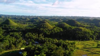Filipinler, Bohol 'daki Chocolate Hills' te bir evde insansız hava aracı ile hava manzarası. Güzel yeşil tepeler ve ağaçlar ufukta, mavi gökyüzünün altında - 4K