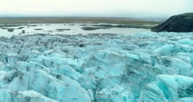 Amazing shot in Iceland takes us behind the horizon capturing mesmerizing winter scenery of a small black volcanic hill set over large glacial sheet with a background of a shallow lake and large virid plains under the clear winter sky.