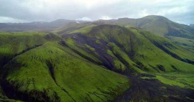 Amazing view of the Icelandic nature with green ridges.. Amazing view of the Icelandic nature showing beautiful mountains and ridges all covered in green. Distant mountains in the background with their tops covered with snow set under cloudy sky.