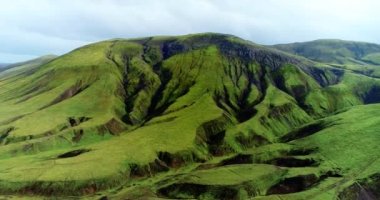 Medium close up shot of hills and ridges all coated with green spring grass and overlooking a riverbed with a small creek of sparkling water flowing. The camera is zooming toward the top of the hill.