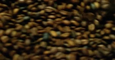 Roasted brown coffee beans rotating in a cooling mixer machine.