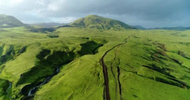 Aşağıdan akan yeşil yosun ve derelerle kaplı canlı lav tepeleri. İnsansız hava aracı yeşil lav tepeleri üzerinde uçarken yeşil yosunlarla kaplanmış ve dereleri akan otlarla ateş ediyor.. 