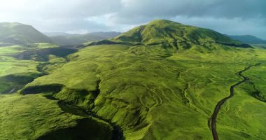Icelandic landscape showing glaring light of the sun in the middle of the sky and clouds gathering desperately to block it. The sun's rays reflect over the silver water of small creeks