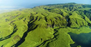 İzlanda 'daki panoramik manzara dağlık arazi ve eteklerdeki göl. Panoramik manzara canlı yeşil tepeler ve tepeler gösteriyor, ve tepeden akan muhteşem suyla küçük bir şelale ve dağ eteklerindeki güzel bir göle dökülüyor..