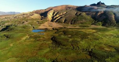 Groups of white geese cross paths on the water's surface. The geese move their wings and fly at a very low altitude as others stay on beach land. The beach is very large and has black volcanic rocky earth. white clouds reaching the horizon.