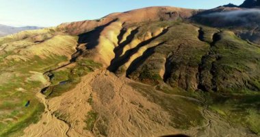 İzlanda 'daki panoramik manzara dağlık arazi ve eteklerdeki göl. Panoramik manzara canlı yeşil tepeler ve tepeler gösteriyor, ve tepeden akan muhteşem suyla küçük bir şelale ve dağ eteklerindeki güzel bir göle dökülüyor..