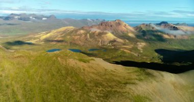 İzlanda 'daki panoramik manzara dağlık arazi ve eteklerdeki göl. Panoramik manzara canlı yeşil tepeler ve tepeler gösteriyor, ve tepeden akan muhteşem suyla küçük bir şelale ve dağ eteklerindeki güzel bir göle dökülüyor..