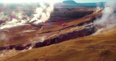 Bir dağın yamacındaki jeotermal deliklerin doğal görüntüsü. Dağ çatlakları büyük bir buluta sülfürik buhar yayar. Güneşin zeminde bir yansıması vardır. Bu da bölgeye güzel bir dokunuş ekler ve onu ısıtır..