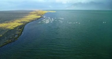 İzlanda 'daki panoramik manzara dağlık arazi ve eteklerdeki göl. Panoramik manzara canlı yeşil tepeler ve tepeler gösteriyor, ve tepeden akan muhteşem suyla küçük bir şelale ve dağ eteklerindeki güzel bir göle dökülüyor..
