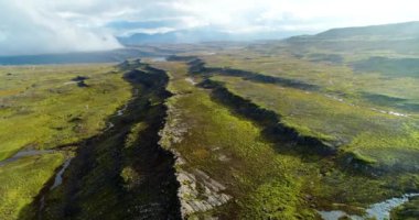 İzlanda 'daki panoramik manzara dağlık arazi ve eteklerdeki göl. Panoramik manzara canlı yeşil tepeler ve tepeler gösteriyor, ve tepeden akan muhteşem suyla küçük bir şelale ve dağ eteklerindeki güzel bir göle dökülüyor..