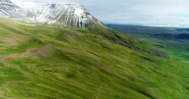 İzlanda dağlarındaki güzel bir şelalenin hava görüntüsü. Nehir, suyu dağın tepesinden onun dibine kadar taşıyor. Dağ yeşil yay çimenleriyle kaplıdır..