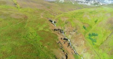 İzlanda 'daki panoramik manzara dağlık arazi ve eteklerdeki göl. Panoramik manzara canlı yeşil tepeler ve tepeler gösteriyor, ve tepeden akan muhteşem suyla küçük bir şelale ve dağ eteklerindeki güzel bir göle dökülüyor..