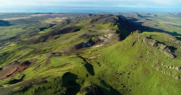 アイスランドの自然の美しさを撮影し 岩の多い丘陵や山々を含む広い芝生の平野で空中撮影し 短い草で覆われた小さな谷 黄金の時間で海の素晴らしい景色を背景に青い澄んだ空 — ストック動画