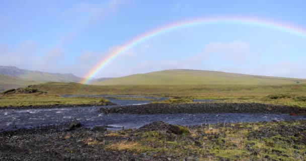 美丽的彩虹在冰原清澈的天空中美丽的彩虹美丽的彩虹风景迷人的彩虹在流淌的河流上形成 黑色的石头和绿色的青草在河岸上形成 背景为群山 — 图库视频影像