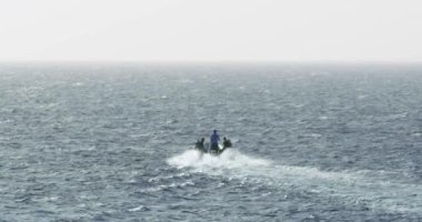 Dağlık bir bölgedeki büyük bir şelalenin manzarası. Şelale çekimin genişliğini doldurur. Şelalenin üstünde yeşil bir dağın altında çimenli bir ova var. Büyük su akıntısı nedeniyle beyaz su köpüğü oluşur..