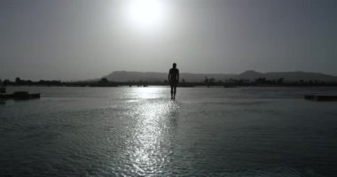 Üstsüz, çekici bir adam, kızgın güneşin altında duruyor ve güneş ışığı, Mısır 'da güzel, sıcak bir yaz gününde üzerine vuruyor. Bronzlaşmış ya da kahverengimsi tenli adam gümüş suya atlıyor..