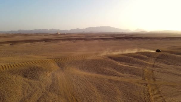 アラビア砂漠に乗っている自動車の空中ショット 晴れた日にエジプトの東砂漠を旅する黒と赤のバギー車 車は荒々しい砂地を行進している 背景には山が連なっている — ストック動画