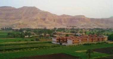 Dağlık bir bölgedeki büyük bir şelalenin manzarası. Şelale çekimin genişliğini doldurur. Şelalenin üstünde yeşil bir dağın altında çimenli bir ova var. Büyük su akıntısı nedeniyle beyaz su köpüğü oluşur..