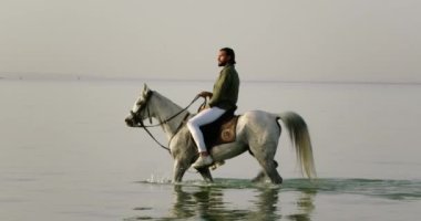 Dağlık bir bölgedeki büyük bir şelalenin manzarası. Şelale çekimin genişliğini doldurur. Şelalenin üstünde yeşil bir dağın altında çimenli bir ova var. Büyük su akıntısı nedeniyle beyaz su köpüğü oluşur..