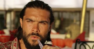 Sigara içen bir adamın yakışıklı yüzüne yakından bir bakış. Güneşli bir günde, arka planı bulanık, güzel bir yerde Chicha tüttüren bir erkeğin güzel yüzünün yakın çekimi.
