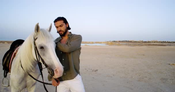 Ένας Όμορφος Άντρας Χαϊδεύει Άσπρο Του Άλογο Δίπλα Στο Νερό — Αρχείο Βίντεο