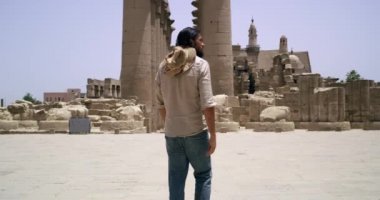 Dağlık bir bölgedeki büyük bir şelalenin manzarası. Şelale çekimin genişliğini doldurur. Şelalenin üstünde yeşil bir dağın altında çimenli bir ova var. Büyük su akıntısı nedeniyle beyaz su köpüğü oluşur..