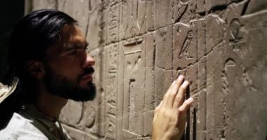 Hiyeroglif sembolleri yakından inceleyen bir turist antik bir duvara kazınmış işaretler, simgeleri yakından inceleyen bir gezgin, temsil ettikleri hiyeroglif sanattan keyif alan, oymalar Mısır 'daki bir arkeolojik alanda yer alıyor.
