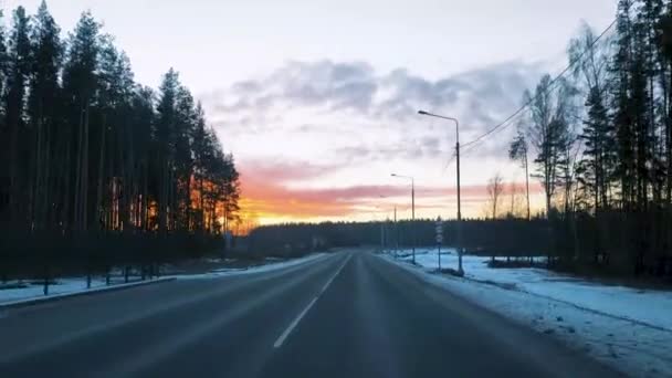 Vista attraverso il parabrezza di una macchina in movimento sulla strada in inverno e una bella alba nel cielo. — Video Stock