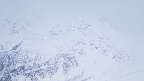 Zwolnij trochę. Strzelanie dronami. Widok z góry na ośnieżony szczyt góry przy wietrznej śnieżnej pogodzie.. — Wideo stockowe