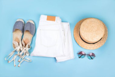 Beyaz kot pantolon, çizgili espadrilles sandaletler, hasır kayıkçı şapkası ve mavi arka planda izole edilmiş kaplumbağa kabuğu güneş gözlüğü ile yaz modası düz yatak..
