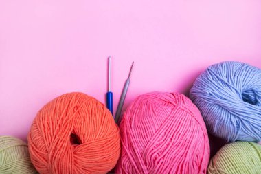 Pembe arka planda iki örgü kancalı çok renkli örgü yumağı..