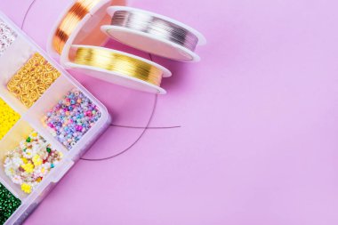 Pembe arka planda mücevher ve tel dizisi yapmak için araçları olan farklı inci boncuklardan oluşan yaratıcı düz tabaka.