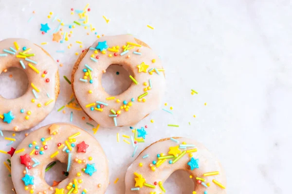 Flatlay of coconut sugar baked donuts decorated with icing and funfetti sprinkles on marble background.