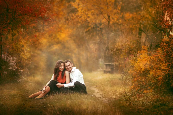 Nádherný pár sedící v podzimním parku a objetí — Stock fotografie