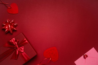 Kırmızı kurdeleli kırmızı hediye kutusu, kırmızı arka planda kalpler ve pembe zarf, aşıklar için romantik sevgililer günü hediyesi.