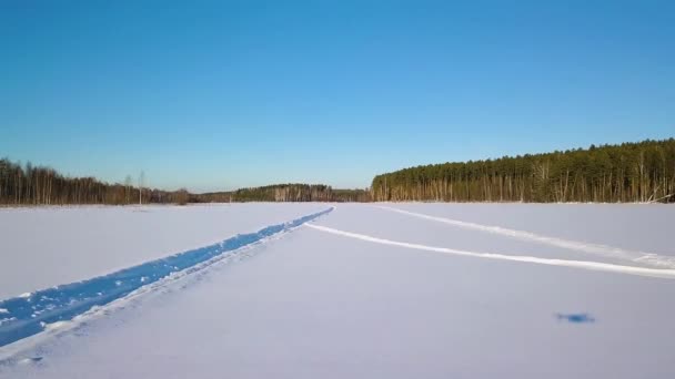Tiefflug über den Schnee mit Spuren. Zugefrorener See. Schatten von der Drohne. Winterklares Wetter. 4K — Stockvideo
