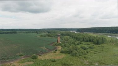 Rusya, Ural. Tarlaların üzerinde uçuyor. Patates yetiştirme sıraları. Eski kırmızı tuğlalı su kulesi. 4K