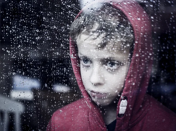 Junge schaut traurig durch Fenster — Stockfoto