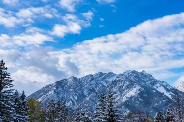 Karla kaplı Norquay Dağı 'nı mavi gökyüzü üzerinde karlı ormanla ve güneşli kış günlerinde beyaz bulutlarla kapatın. Banff Ulusal Parkı. Güzel manzara. Kanada Kayalıkları, Alberta, Kanada.