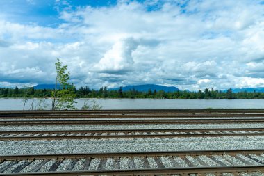 Nehir kıyısındaki tren yolu, mavi gökyüzü beyaz bulutlar üzerinde..