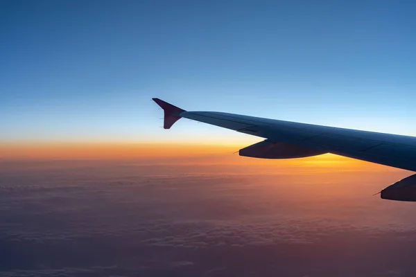 Up in the air, view of aircraft wing silhouette with dark blue sky horizon and cloud background in sun rise or sunset time from airplane window.