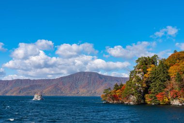 Lake Towada Gezi Turları. Güzel görünümü, berrak mavi gökyüzü, beyaz bulut, sonbahar yeşillik sezon arka plan ile güneşli bir günde yolcu gemisi. Aomori, Japonya. Gemide Japonca Metin 