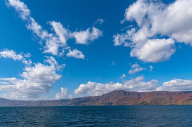 Güzel sonbahar yeşillik manzara manzaralar. Sonbahar muhteşem renklerle doludur. Towada Gölü gezi Cruise gemi görünümü. Berrak mavi gökyüzü, su, beyaz bulut, güneşli bir gün arka plan. Aomori, Japonya