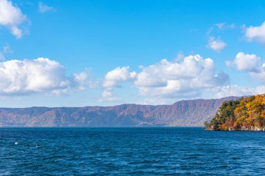 Güzel sonbahar yeşillik manzara manzaralar. Sonbahar muhteşem renklerle doludur. Towada Gölü gezi Cruise gemi görünümü. Berrak mavi gökyüzü, su, beyaz bulut, güneşli bir gün arka plan. Aomori, Japonya