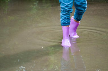 Mor lastik çizmeli bir kız çamurlu su birikintilerinde oynuyor..