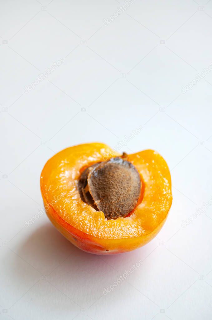 A ripe cut apricot with a seed on white background.