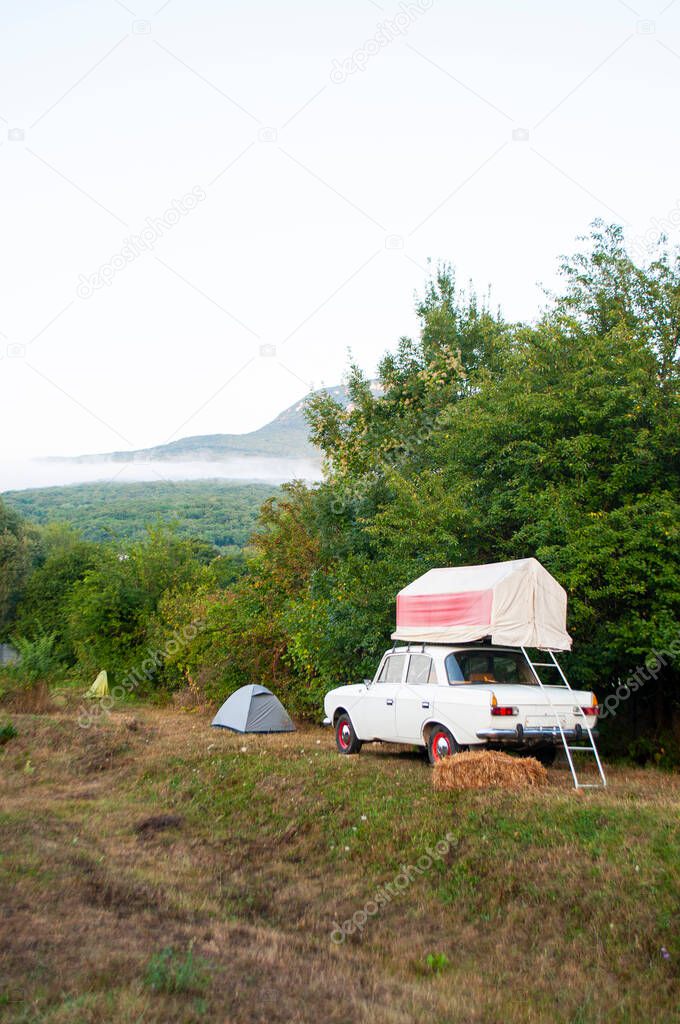 Tent setup on the old retro car among trees with view of mountains.