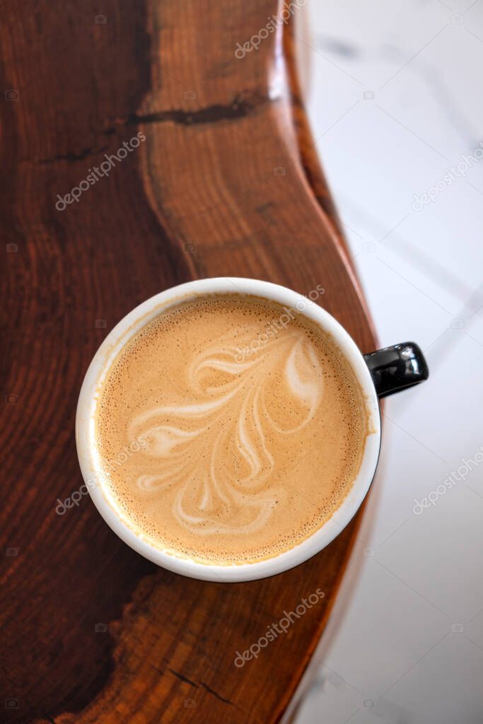 Freshly served cup of cappuccino with latte art on a wooden table in a cafe.